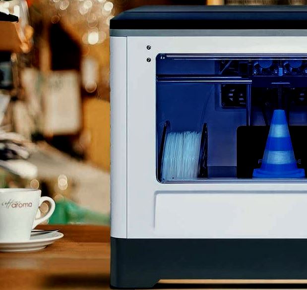 A Flashforge Dreamer at home next to a cup of coffee